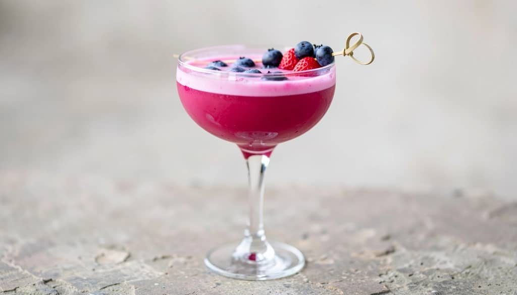Strawberry blueberry margarita in a coupe glass with berry garnish